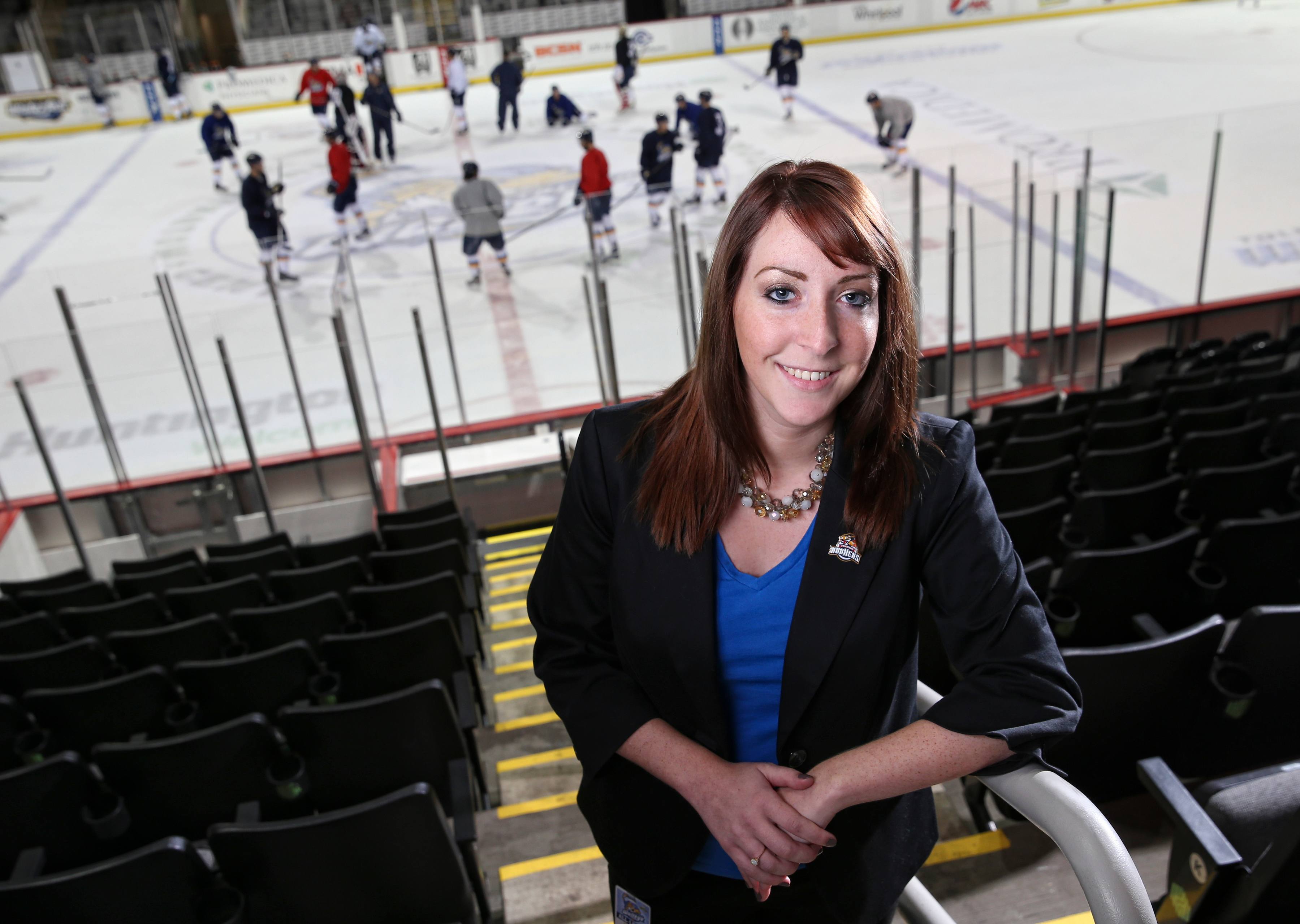 Morgan-Carlson-8628c A woman in the BGSU sport administration master's program stands in the bleachers of a hockey rink as players practice on the rink behind her.